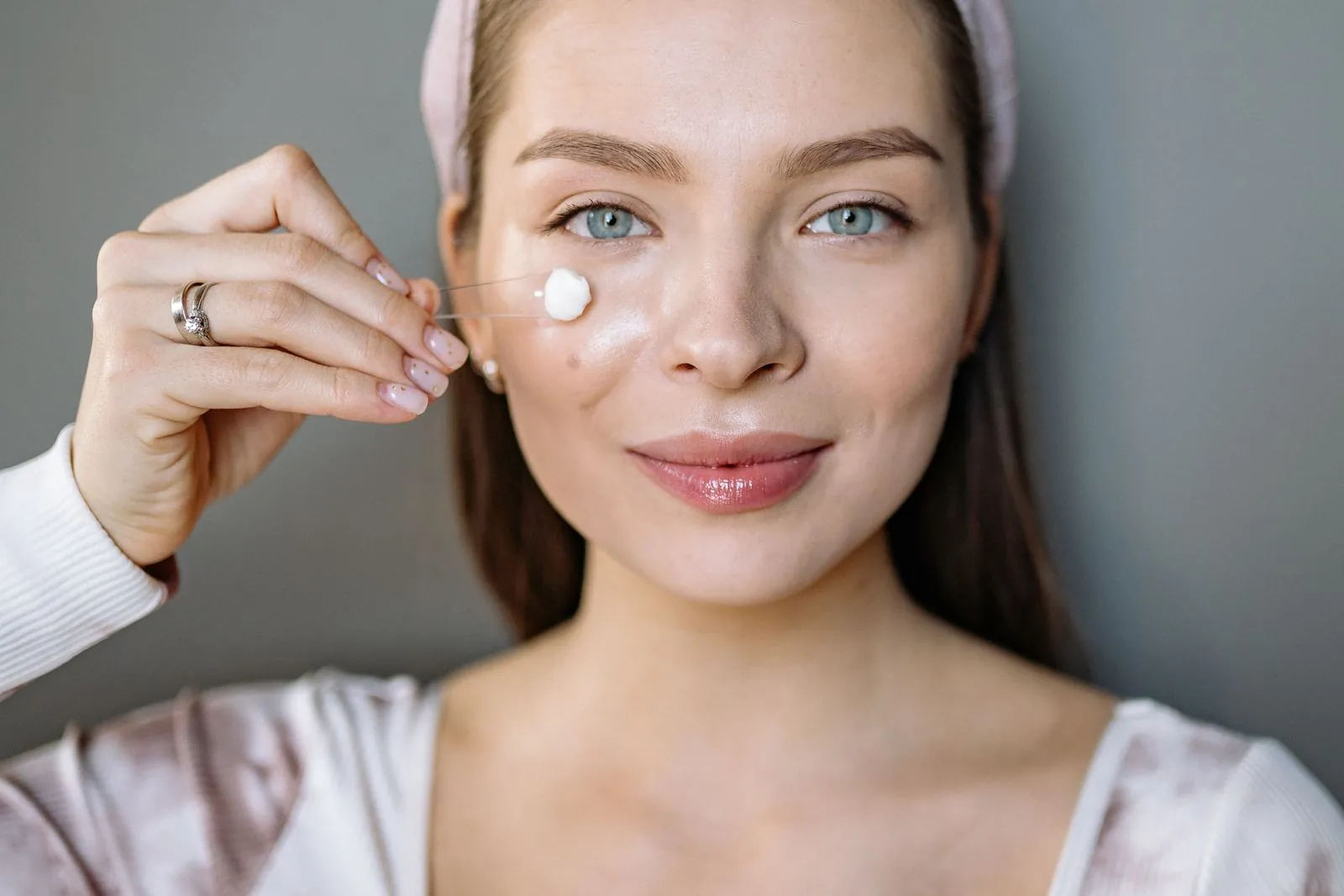 Woman dabbing a small amount of white cream onto her cheek with one fingertip