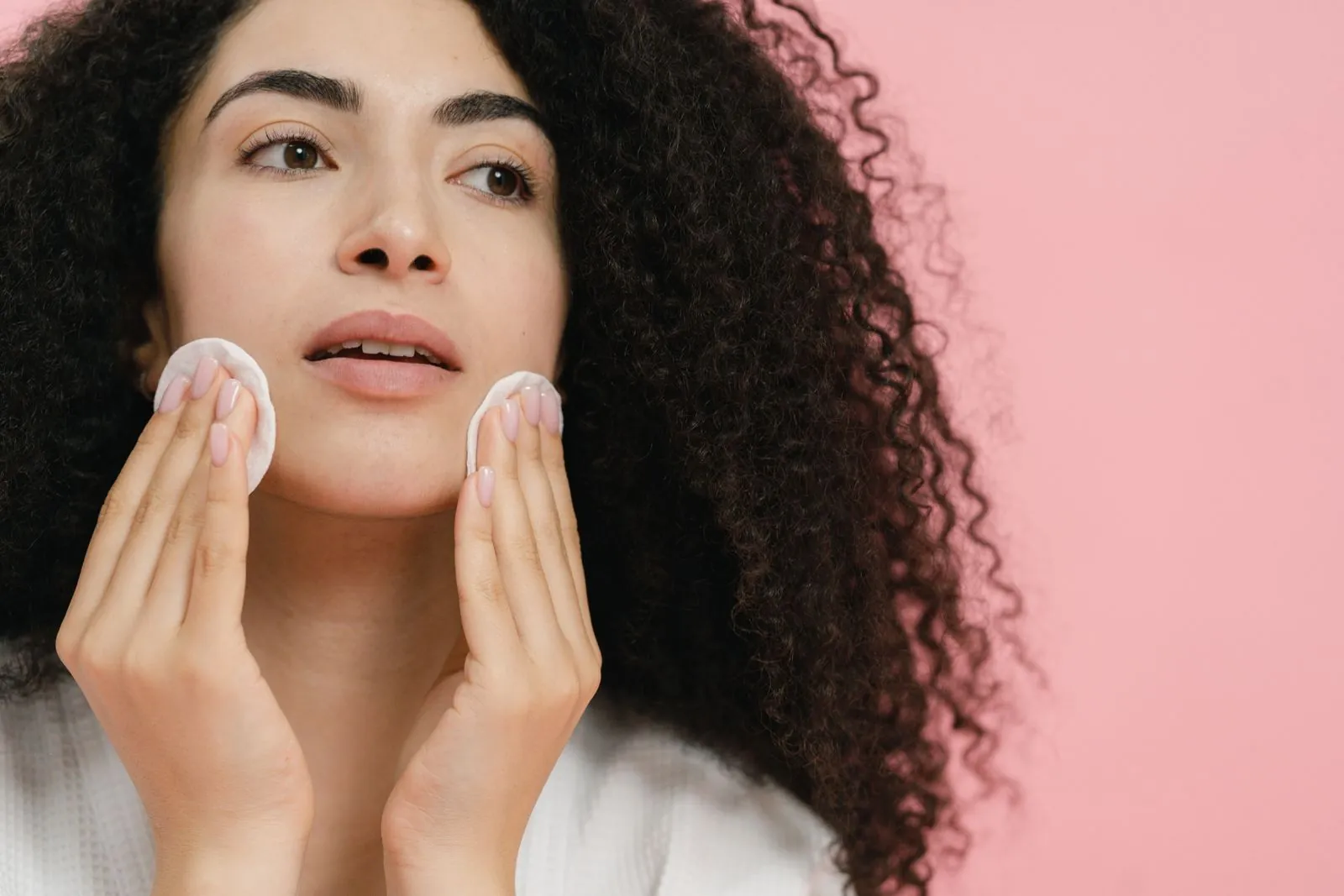 Woman pressing a cotton pad to each cheek during her skincare routine