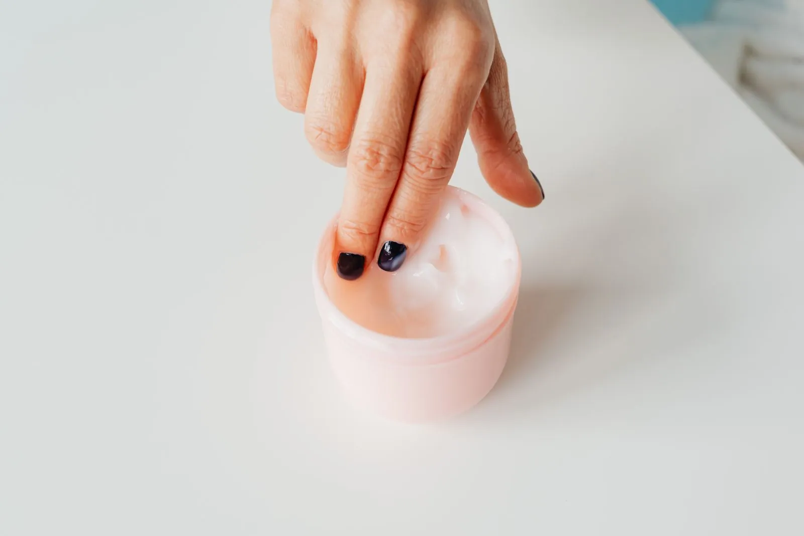 Fingertips dipping into an open jar of thick white face cream