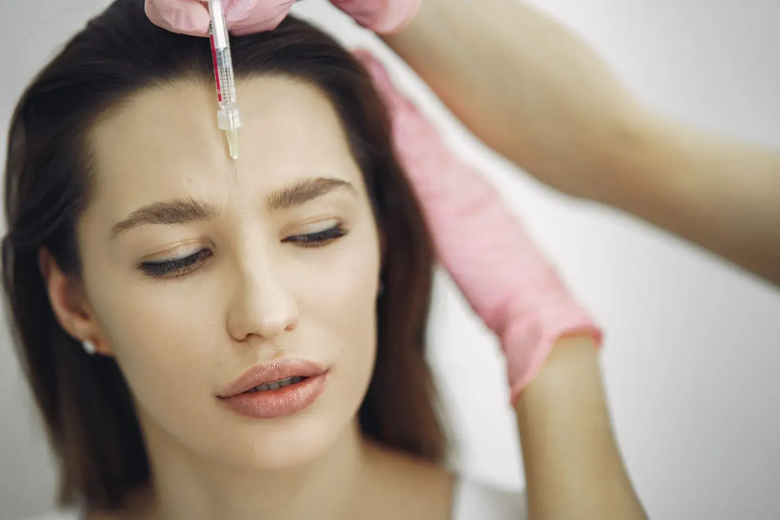 Injector placing a small dose of Botox into a woman's forehead