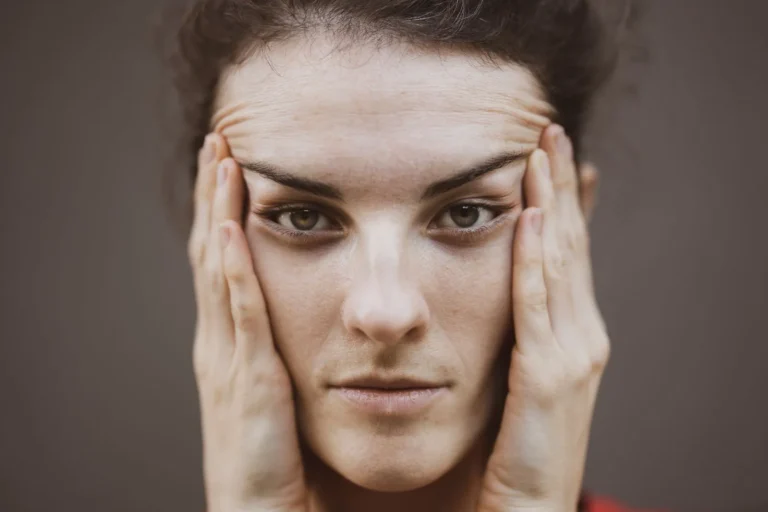 Woman pressing her hands to her temples, pushing her forehead up into horizontal lines