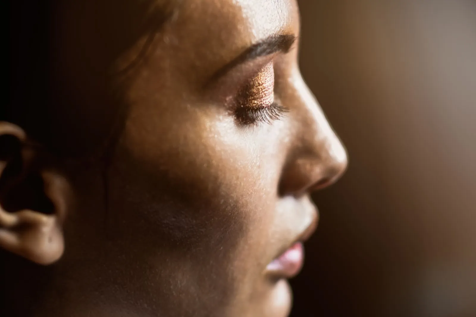 Close-up side profile of a woman's cheek catching light, with a dewy sheen and visible pores