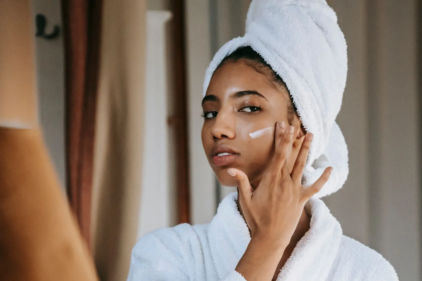 Woman in a bathrobe applying a dab of moisturizing cream to her cheek