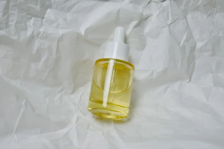 Unlabeled glass dropper bottle of pale yellow face serum on white crinkled paper
