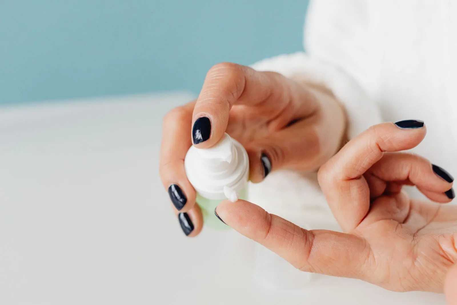 Hand pumping a small dab of white cream from an unbranded bottle onto a fingertip