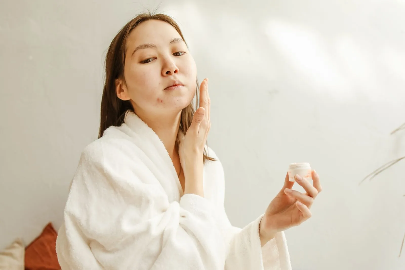 Woman in a white robe dabbing a small amount of cream onto a blemish on her cheek