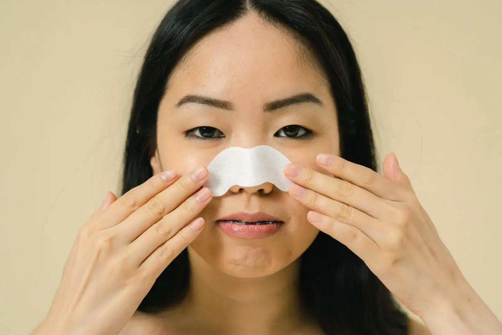 A woman pressing a white pore strip onto her nose