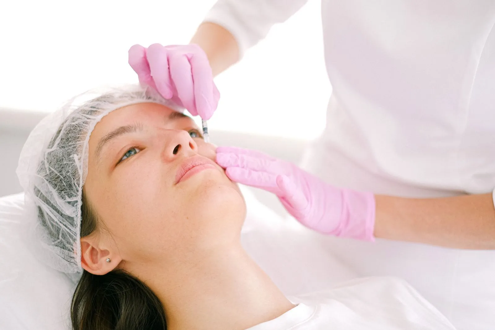 Injector placing a small cosmetic injection beside a woman's nose bridge