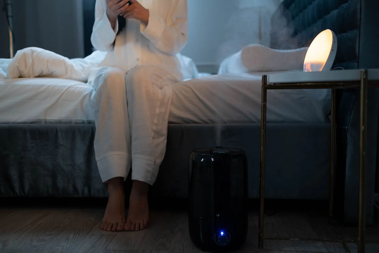 A humidifier releasing mist beside a bed in a dim bedroom