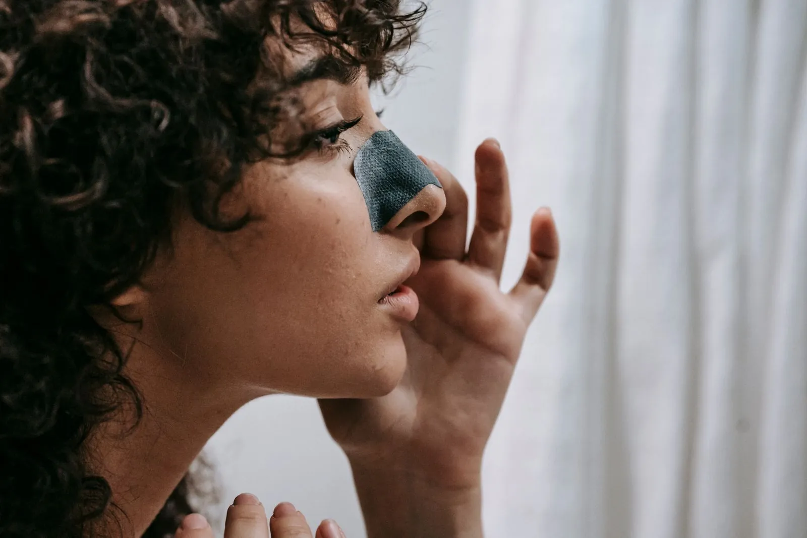 Woman wearing a charcoal pore strip across her nose, seen from the side