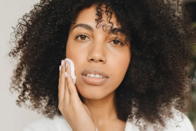 Woman with curly hair pressing a cotton pad soaked in toner gently against her cheek